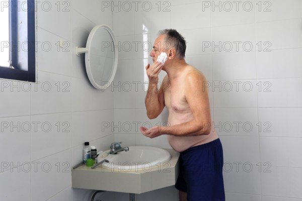 Man 60 plus shaves wet in the bathroom