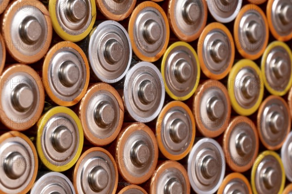 Multiple used AA alkaline batteries are seen arranged in a pile. Closeup side view from the plus side of the battery