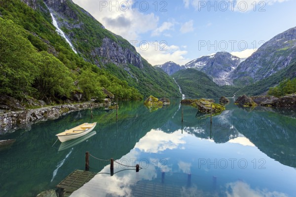 The mountain lake Bondhuswatnet. The boat is reflected in the clear water of the lake. Gorgeous Norway. Emerald green of summer grass
