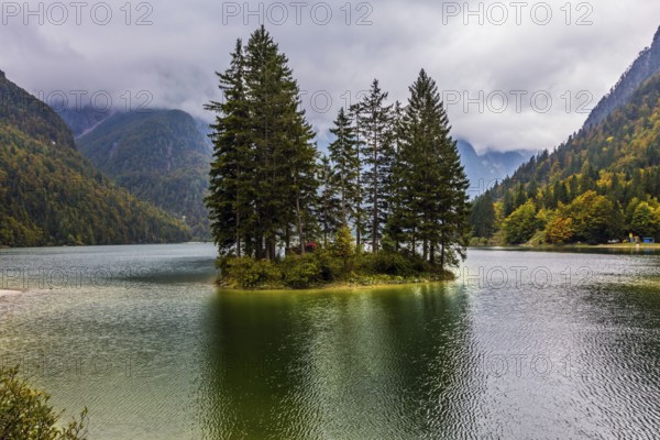 The surface of the lake Di Predil is covered with light ripples. Cold autumn in the Alps. Small island in the middle of the lake. The concept of active, mountain, environmental and photo tourism