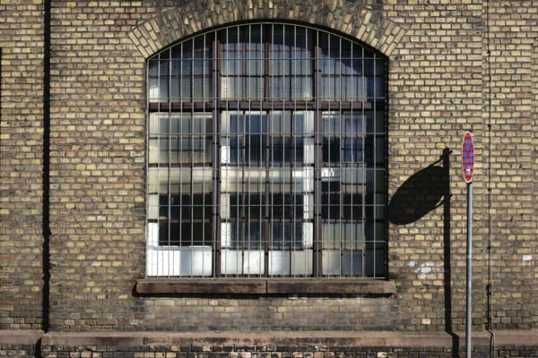 A no stopping sign casts a shadow on the brick wall on the disused industrial site of an old factory with a barred window