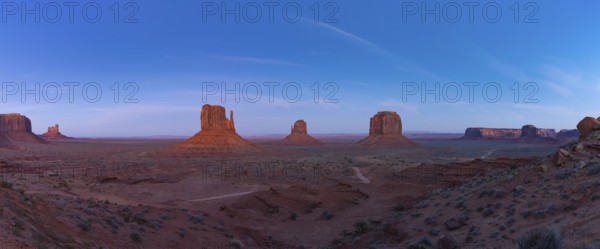 A panorama picture of the Monument Valley landscape in the early evening or night, with the West Mitten Butte, East Mitten Butte and Merrick Butte rock formations in the center