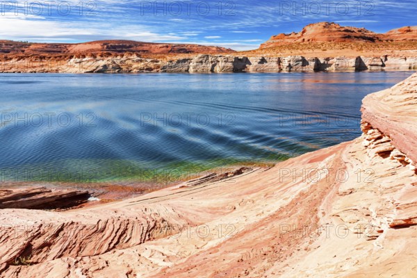 The smooth emerald water of the lake contrasts with the bright red terracotta sandstone shores. Lake Powell. USA. The coast is cut by narrow canyons