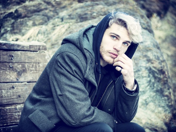 Portrait of young man in hoodie posing outdoor in winter setting with snow all around, looking at camera
