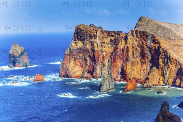 The west coast of the island of Madeira - red rocks, turquoise surf. The blinding midday sun illuminates the rocky shore. The concept of active, ecological and photo tourism