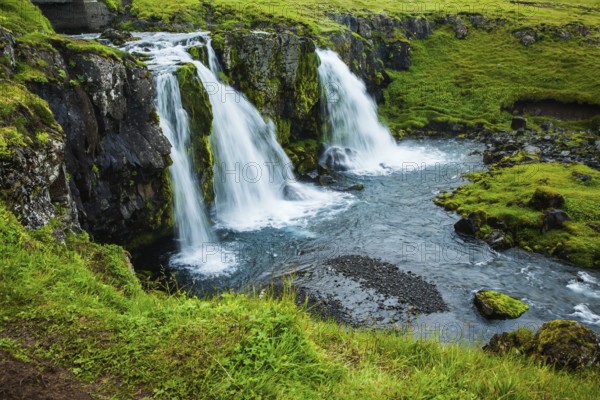 Cascading waterfall Kirkjoufellfoss at the foot of the mountain Kirkjoufell. Summer in Iceland. Concept of exotic and extreme tourism