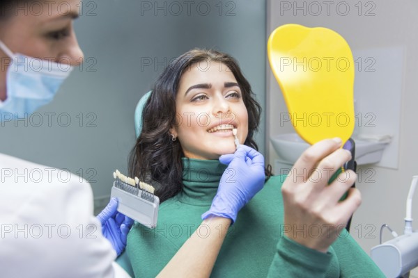 Female dentist, patient holding mirror. Tooth shade chart