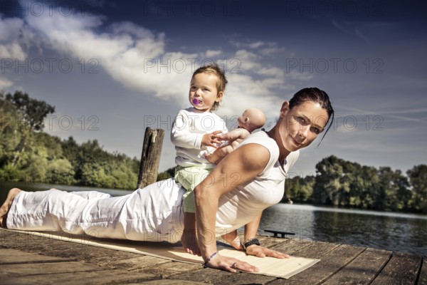 Young woman and her little daughter making yoga exercise at a lake