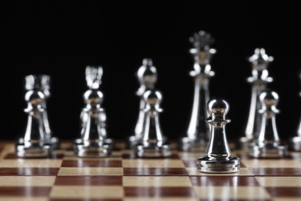 Steel chess figures standing on wooden chessboard. Intellectual duel and tactical battle in business. Strategy planning and leadership concept. Silver metal chess pieces in row on black background