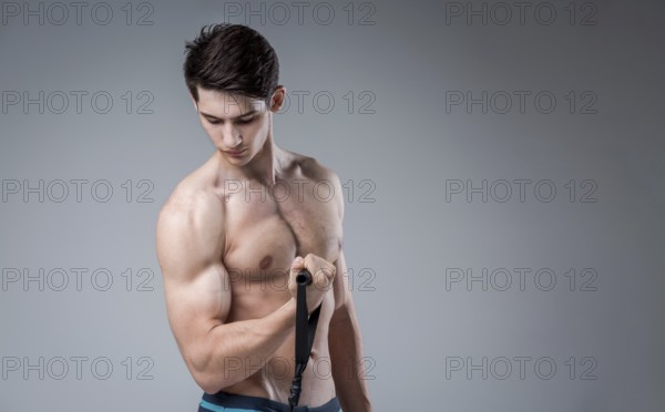 Muscular fit young male antique perfect muscles six packs of abs and bare chest. Bodybuilder model trains with a stretching elastic against a dark background in the studio. Workout training gym