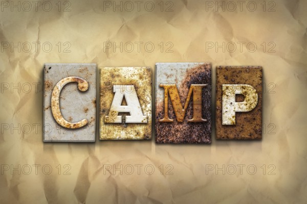 The word CAMP written in rusty metal letterpress type on a crumbled aged paper background