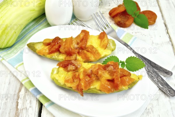 Young zucchini baked in a flavored sauce with dried apricot, cream and cheese in a bowl on a towel on the background of wooden boards