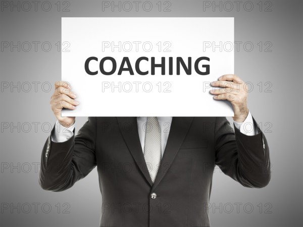 A business man holding a paper in front of his face with the message coaching