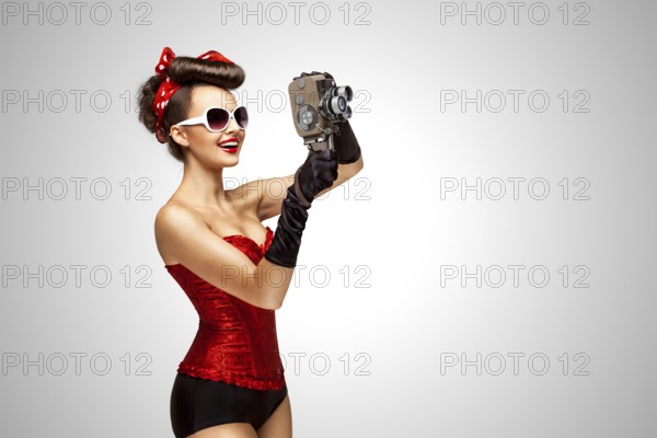 Retro photo of a pin up girl with an old 8 mm camera on a grey background