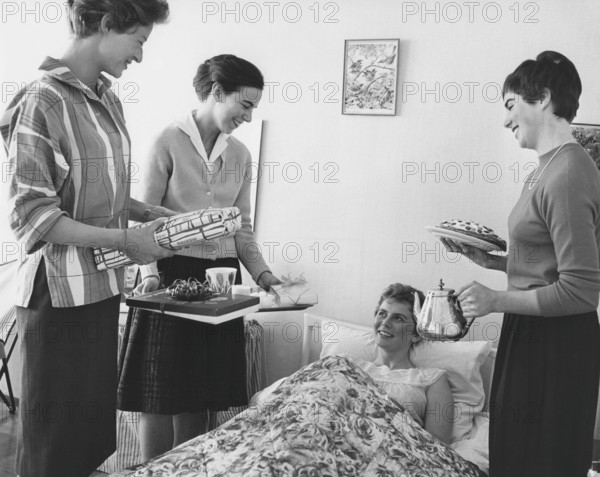 Birthday in the 1960s. A young woman lies in bed and is surprised by her girl friends singing happy birthday to you. They have all three wrapped presents ready. A coffee tray and coffee from a silver pot and cake are also included. Sweden 1961