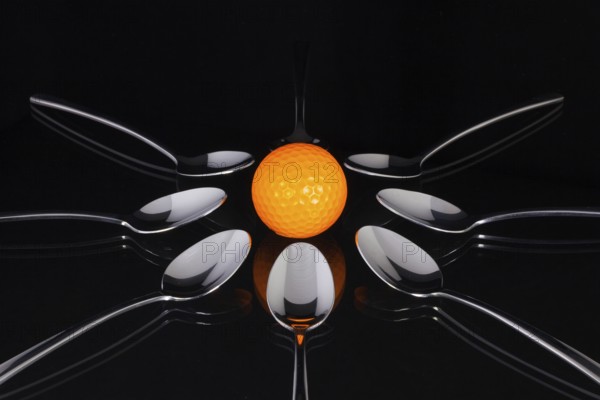 Teaspoons and orange golf ball on the black glass table