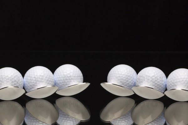 Six spoons and golf balls on a black glass desk
