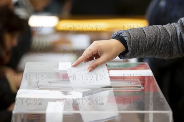 A woman casts her envelope vote into a transparent plastic ballot box. Human hand voting