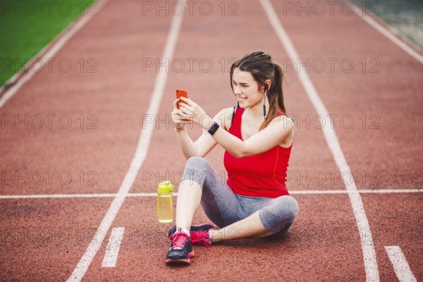 Beautiful fitneß girl uses smartphone at stadium after workout. Sports and healthy. Sport woman use of cellphone inside sport complex. Sport and technology. resting after workout, run at red track