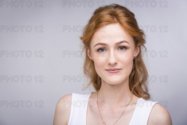 Portrait of a beautiful young woman of European, Caucasian nationality with long red hair and freckles on her face posing on a white background in the studio. Close-up student girl in a white blouse