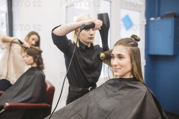 Portrait of happy woman at the hair salon. Professional hair styling concept. Hairdresser drying girl long hair using hairdryer and brush. Drying With Blow Dryer