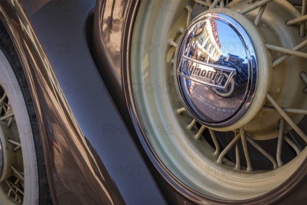 Lisbon, Portugal - Sep 29, 2024: Close-up and selective focus of spare wire wheel and wheel center cap with Plymouth logo on sunny day. Urban setting reflections, vintage look. Plymouth Chrysler motors, Chrysler Corp, USA, North America