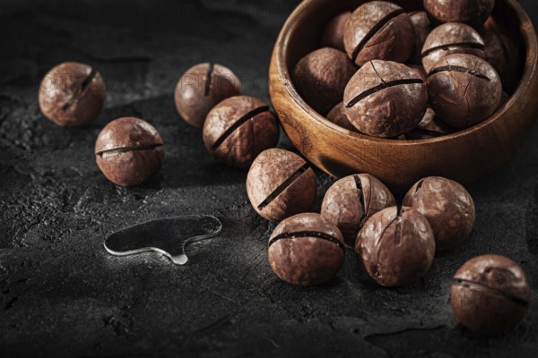 Macadamia Nuts And Key For Open It With Wooden Bowl On Black Background