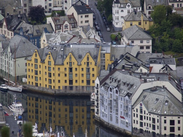 Yellow and white houses are reflected in the canal, surrounded by several small boats, alesund, norway
