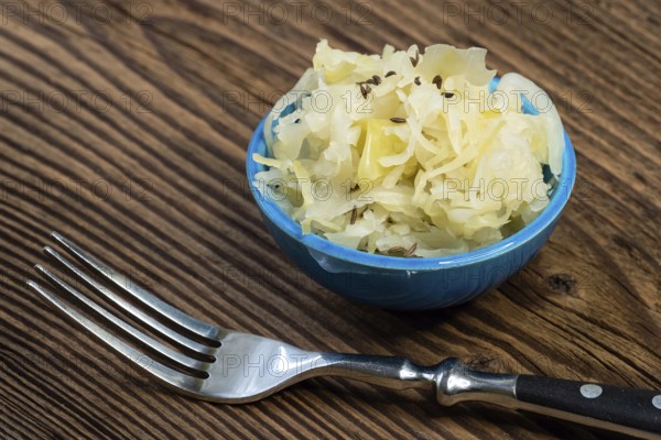 Homemade pickled sauerkraut in a bowl with a fork on a wooden board