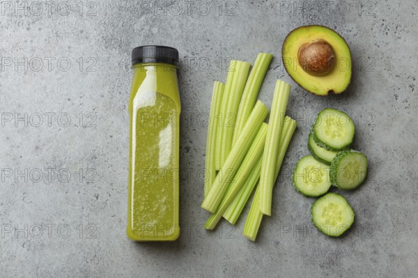 Bottle of green vegetable smoothie with fresh celery sticks, cut avocado, cucumber on gray concrete background top view. Diet beverage, healthy nutrition, detox cocktail, food photography, food photography