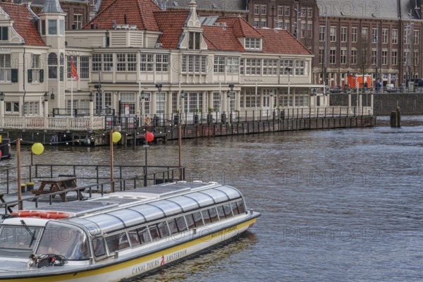Houseboat in front of a historic building with red roofs on the canal, Amsterdam, Netherlands