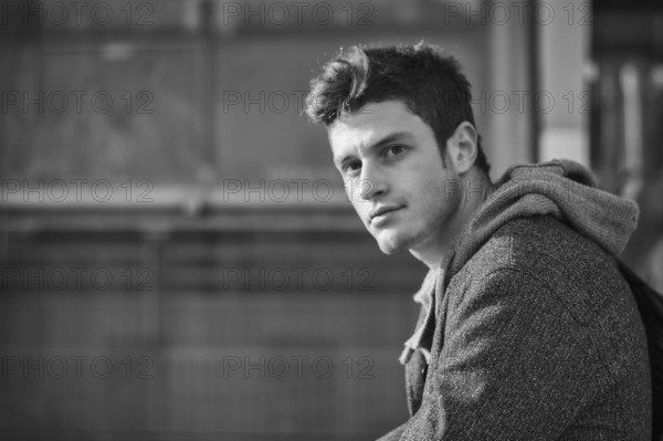 Handsome young man in city setting, lit by sunset light, looking at camera in a black and white shot