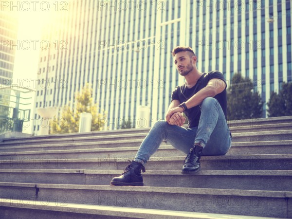One handsome young man in urban setting in European city, wearing jeans and black t-shirt