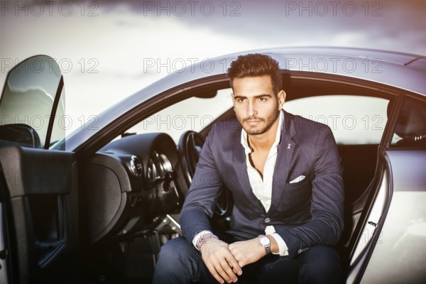 Portrait of young attractiave man in business suit sitting in his new stylish car outdoor in countryside