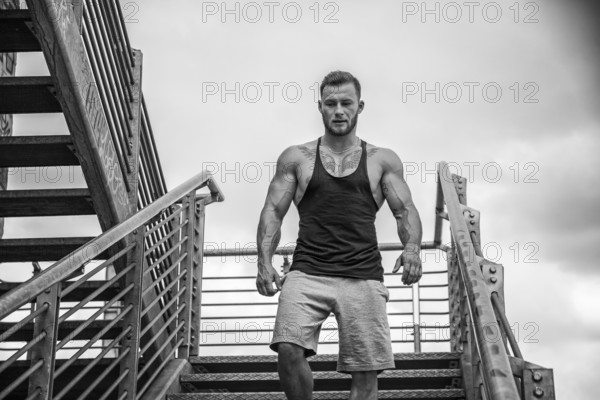 Handsome muscular man standing in city setting looking away to a side, walking down metal stairs