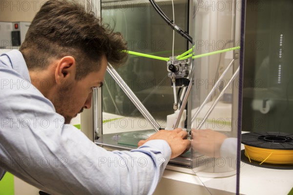 Brunet adult man working with 3D printer, observing the machine at work