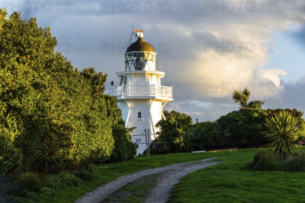 Snow-white picturesque lighthouse at sunset on the Pacific Ocean. South Island, New Zealand. Southern Scenic Route. The concept of environmental and photo tourism