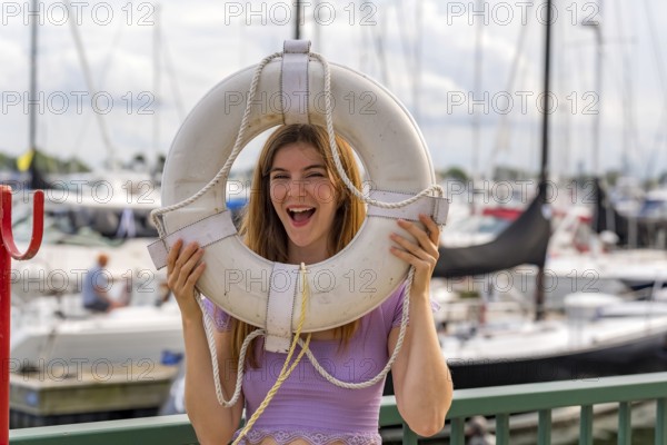A gorgeous redhead model enjoys the perfect summer weather at a local marina, surrounded by boats of all kinds in the background, their reflections dancing on the water under the bright, sunny sky, Milwaukee, United States of America