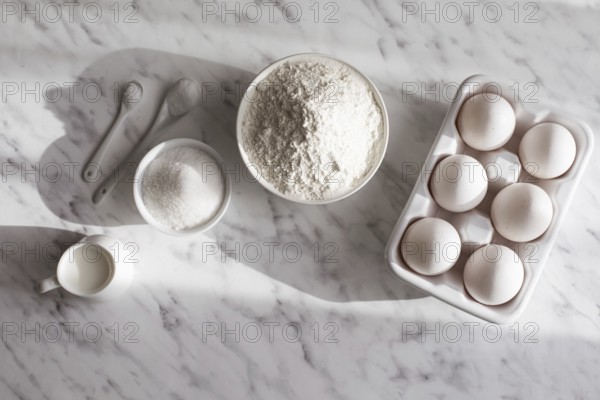 Top view ceramic tray with eggs placed near bowl of flour and sugar. White utensils with white ingredients on white surface. Copy space