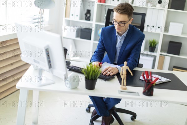 A handsome young man with glasses, a blue suit and a light shirt is working in the office. photo with depth of field