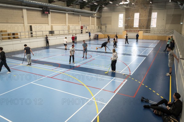 February 21, 2019. Denmark. Copenhagen. Team game with stick and ball Floorball or hockey in hall. Inside training in the gym of the school college. Group of teen caucasian students playing a game