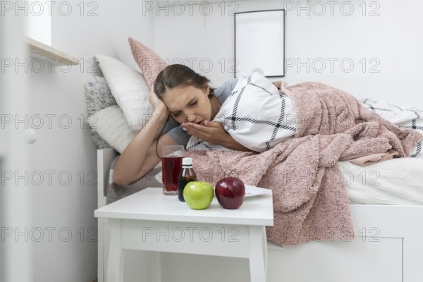 On the bed lies a teenager and in front of her stands a table with apples and medicines that must be swallowed