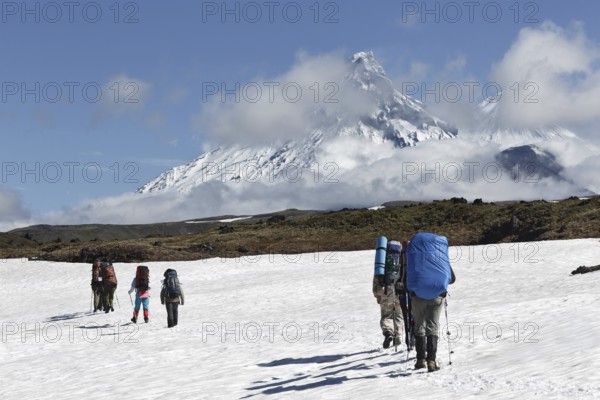 Hiking on Kamchatka Peninsula: hiker goes in mountain on background of Klyuchevskaya group of volcanoes: Kamen Volcano, active Klyuchevskoy Volcano and active Bezymianny Volcano on sunny day. Russian Far East, Kamchatka