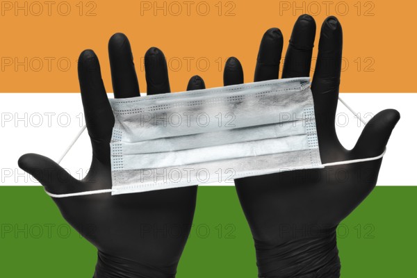 Doctor holds face mask in hands in black medical gloves on background colors National Flag of India. Pandemic insurance coronavirus, flu, airborne diseases. Human medical respiratory mask