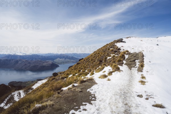 A mountain path with snow offers an impressive view of a lake and mountains, Roys Peak, Wanaka, New Zealand, Oceania
