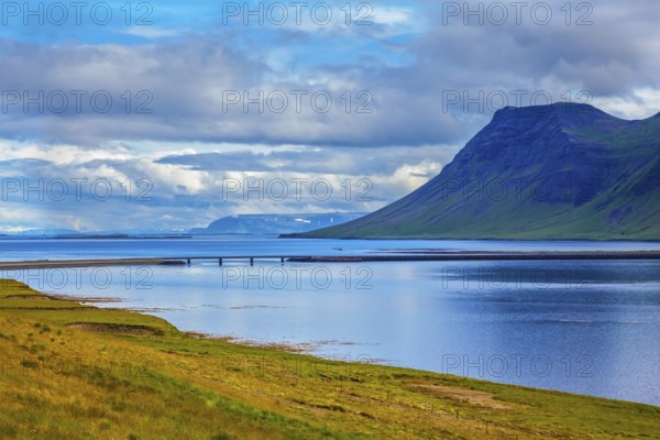 Smooth water of the cold fjord reflects clouds. Cold summer in Iceland