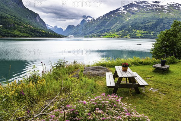 Wooden table and benches on the banks of the picturesque Lovatnet. Northern Europe in July. Summer trip to Norway. Warm cloudy day