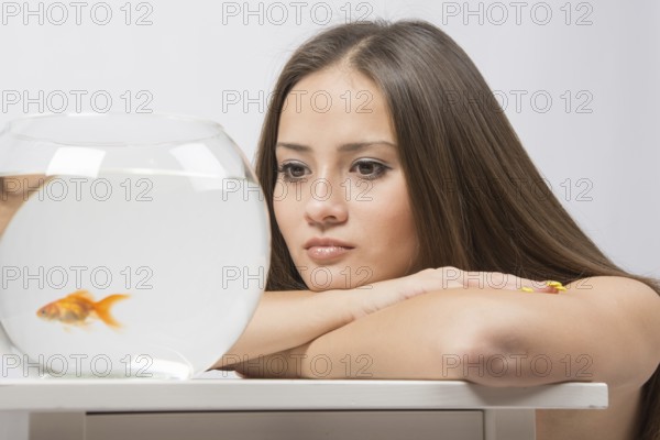 A young girl sits next to a round aquarium in which swimming goldfish