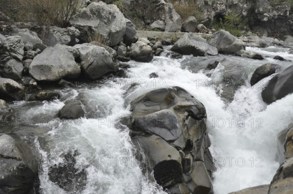 Whitewater rapids swirling around large rocks in a river, The Alcantara Park is located on the northern slope of Mount Etna, between the provinces of Messina and Catania in Sicily. The Alcantara gorges were created by the waters of the river flowing through lava flows from Mount Etna. The park is home to several plant species, including plane trees, oaks, willows and oleanders, and a variety of animals, including migratory birds, mammals and fish
