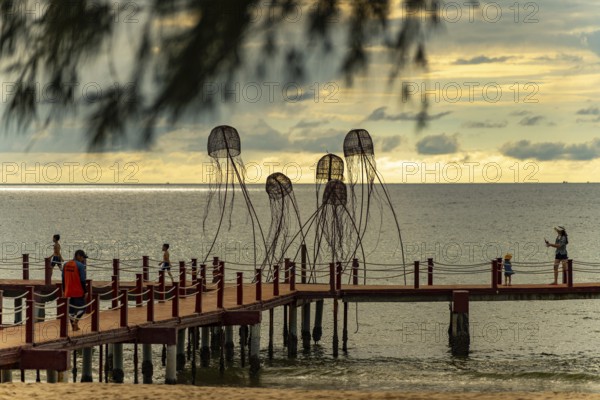 Families walking on a pier with jellyfish sculptures at a peaceful ocean sunset, sun, sunset, beach, sand, sculpture, clouds, Sunset Sanato Beach in Phu Quoc island in Vietnam